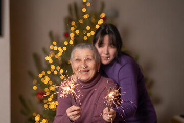 Burning bengal lights in the hands of woman and girl against the background of a Christmas tree. Merry Christmas and New year celebration. 