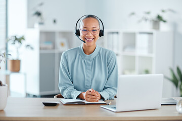 Happy and confident call center agent sitting in front of a laptop while wearing a headset in an...