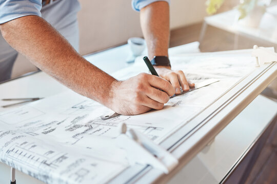 Male architect hands drawing building project or construction plan on an office table. Closeup of caucasian man taking measurement notes, sketching and making corrections to a blueprint.