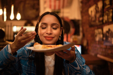 Hungry woman with delicious pizza, food or consumables at a bar, restaurant or diner at night. One...