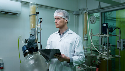 Scientist holding paper board and checking rotational vaporizer during CBD oil extraction, hemp oil...