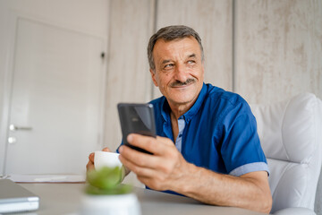 senior man hold cup of coffee and mobile phone while sitting at work