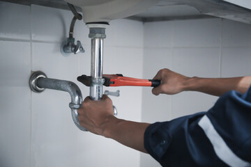 Male Plumber Using Wrench To Fix Leaking Sink In Home Bathroom.