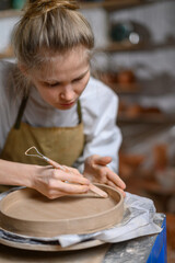 Fototapeta na wymiar A ceramist makes a plate. Woman in an apron works in a pottery workshop. 