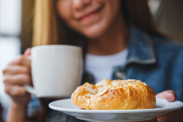 Obraz na płótnie Canvas Closeup image of a young woman drinking coffee and eating a fresh almond croissant