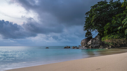 Fototapeta na wymiar Beautiful tropical beach. Calm turquoise ocean and clean sand. Picturesque boulders and green vegetation at the water's edge. Clouds in the sky. Seychelles. Mahe Island. Beau Vallon Beach