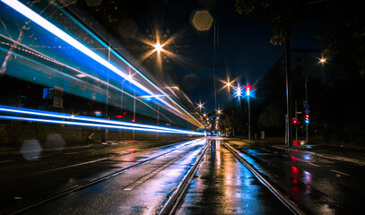 long exposure traffic trails in night city scene with wet floor reflections and traffic lights in the background and rails on the ground