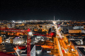 night shot of a crane and urban city with bright lights with long exposure traffic and car lights -...