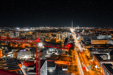 Obraz premium night shot of a crane and urban city with bright lights with long exposure traffic and car lights - berlin by night with the tv tower in the background