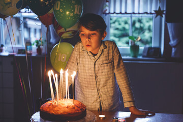 Adorable happy blond little kid boy celebrating his birthday. Child blowing candles on homemade...