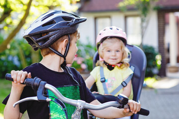 Obraz premium Portrait of little toddler girl with security helmet sitting in bike seat of brother. Kid boy on bicycle with lovely sister. Safe and child protection concept. Family weekend activity trip.