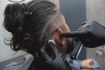 A barber uses an alcohol soaked cotton ball to moisturize and clean the back of a customer's ear...