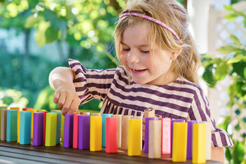 Little preschool girl playing board game with colorful bricks domino. Happy child build tower of...