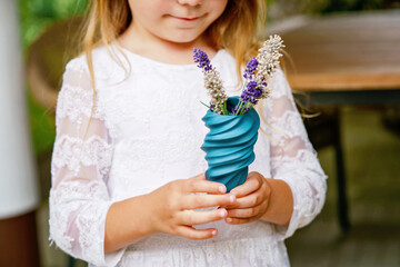 Little preschool girl with flower lavender bouquet at home. Happy child holding a small vase