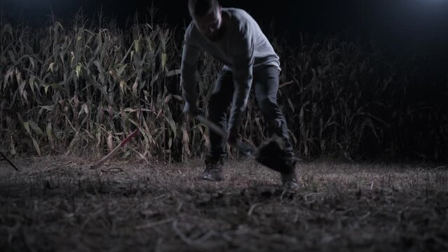 Killer digs grave at night. Young scary man digs hole in fieldl. Long shot. Halloween concept.