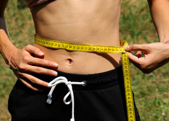 skinny girl measuring her waist with a yellow measuring tape