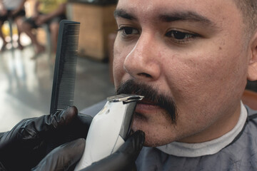 A barber uses a cordless t-blade trimmer and fine comb to contour and trim the lower edge of the...