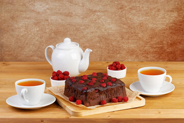 Homemade cake with raspberries and two cups of tea on wooden table. Copyspace.