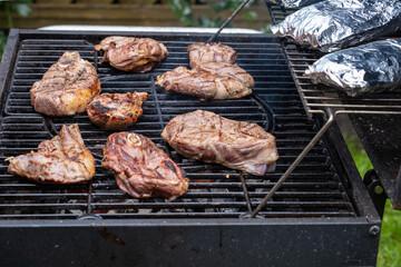 Pieces of fresh meat and fish in foil are laid out on a grill grate. Barbecue cooking. Selective focus.