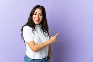 Young caucasian woman isolated on purple background surprised and pointing side