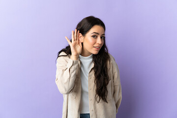 Fototapeta premium Young caucasian woman isolated on purple background listening to something by putting hand on the ear