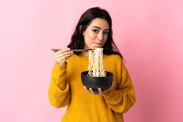 Young caucasian woman isolated on pink background holding a bowl of noodles with chopsticks