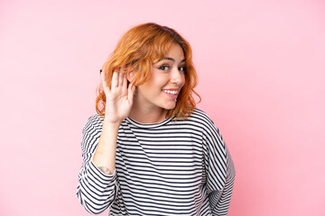 Young caucasian woman isolated on pink background listening to something by putting hand on the ear