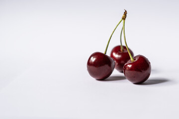 Three cherries are placed on a light background with negative space