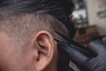 Closeup shot of a barber using a sharp pair of scissors to trim the hair behind the ears. Finishing...