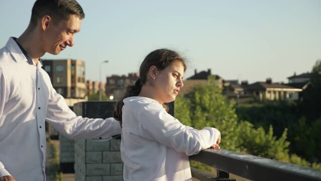 Young man with cerebral palsy comes to stylish disabled woman on bridge. Couple stands on bridge smiling to each other. Sun lights faces of lovers on sunny day