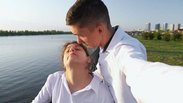Young man with cerebral palsy records video of bright moments. Young couple spends time together looking at river from bridge. Man and woman smile to each other