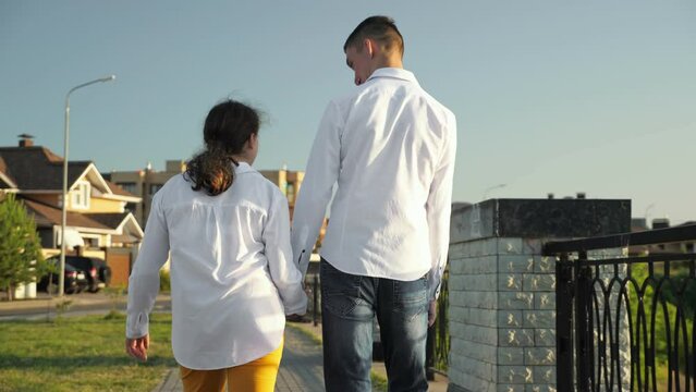 Couple of young people with cerebral palsy in white shirts walks in town talking about funny moments. Man and woman enjoy moments together back view