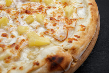 Pizza with meat, ham, pineapples, on a wooden round board on gray concrete