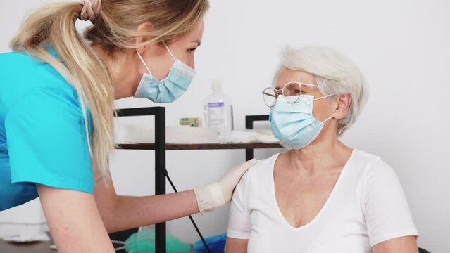 Senior lady with grey hair and her glasses on smiling sincerely at the doctor while wearing a face mask during a medical checkup. High quality 4k footage