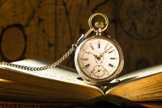 Antique pocket watch on opened old book. Old map on background.