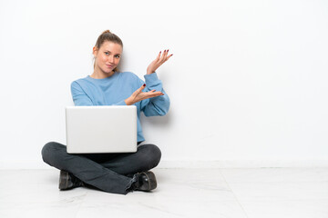 Young woman with a laptop sitting on the floor extending hands to the side for inviting to come