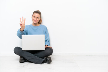 Young woman with a laptop sitting on the floor happy and counting three with fingers