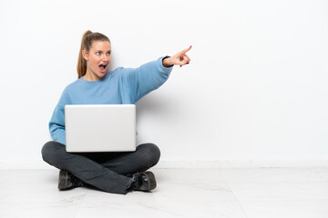 Young woman with a laptop sitting on the floor pointing away