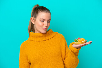 Young caucasian woman holding a tartlet isolated on blue background with sad expression