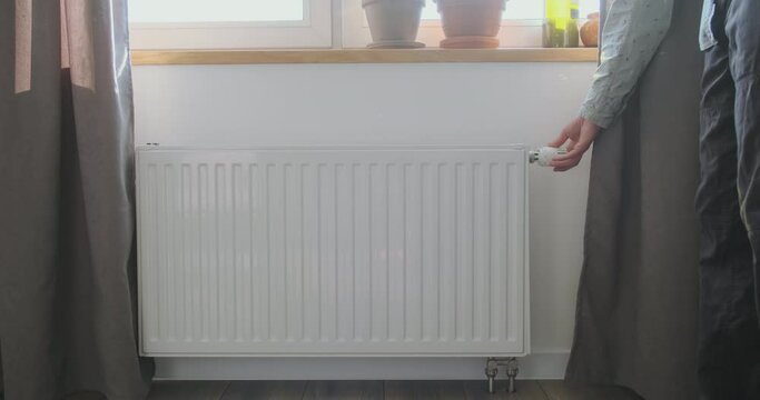 Man goes to the window and turns off the battery radiator thermostat. Front view. The concept of saving gas, heating the apartment, reduce the cost of heat carriers.
