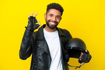 Young Brazilian man with a motorcycle helmet isolated on yellow background showing ok sign with fingers