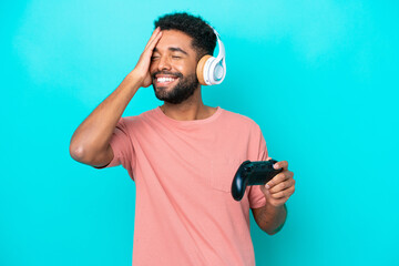 Young brazilian man playing with a video game controller isolated on blue background smiling a lot