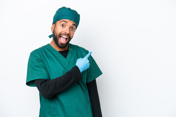 Surgeon Brazilian man in green uniform isolated on white background surprised and pointing side