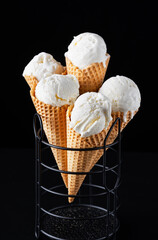Close up view of delicious vanilla ice cream in crispy waffle cone on black background
