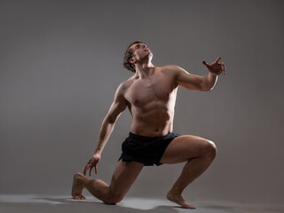 Obraz premium Muscular man in an artistic pose, portrait on a gray background. The guy is an athlete with spectacular muscles in a dramatic pose.