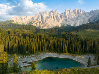 Fototapeta na wymiar Stunning view of Carezza Lake (Lago di Carezza) with its emerald green waters, beautiful trees and mountains in the distance during a dramatic sunset.