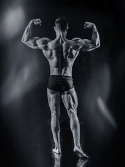 Fototapeta na wymiar Handsome bodybuilder doing classic back double biceps pose, looking away, on dark background