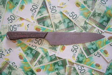 Money with knife. Knife on pile of new Israeli money bills (banknotes) of 50 shekel background