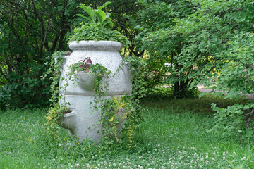 Antique stone vase with garden flowers in a summer park.