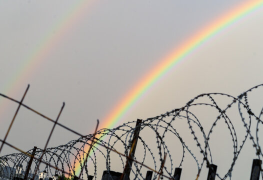 Double rainbow behind rows of a barbed wire. LGBTQ freedom suppression concept.
